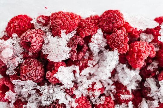 close up of frozen raspberries with ice crystals in clear container