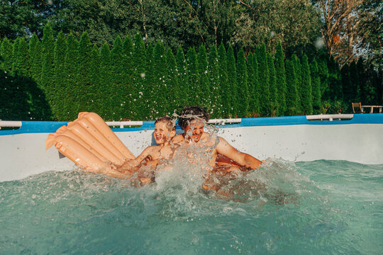 Father and son splashing water in wading pool at backyard