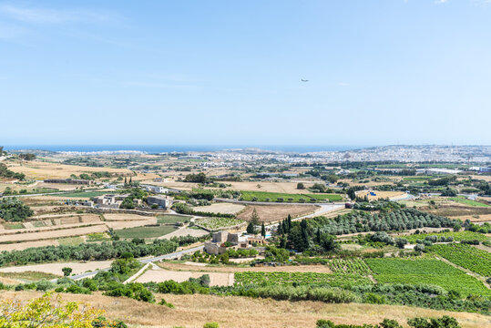 Panoramic landscape of central Malta viewed from the fortified walls of Mdina, featuring farmland, vineyards, rural villages, and the Mediterranean coastline.