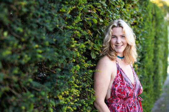 A smiling woman stands outdoors next to a green hedge in Berlin