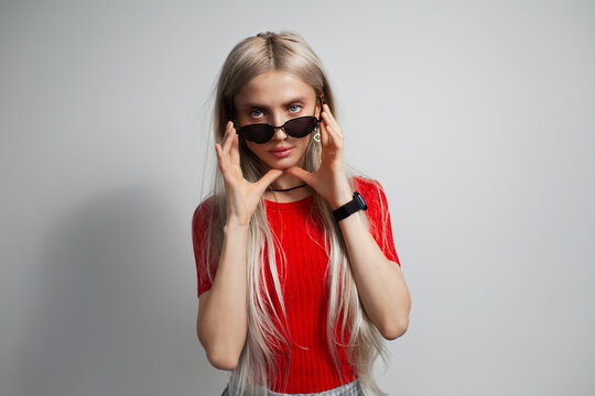 Young pretty blonde girl in red shirt wearing sunglasses isolated on grey background.