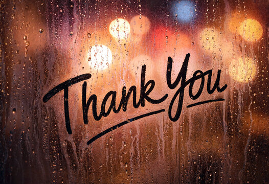 Thank you written on a rainy window with water droplets and warm bokeh lights in background