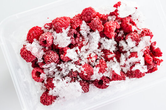close up of frozen raspberries with ice crystals in clear container