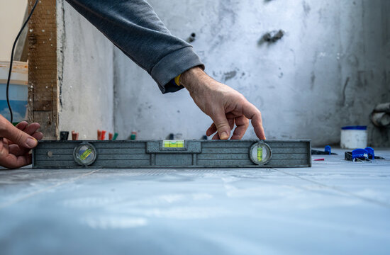 Worker carefully leveling newly laid tiles on a bathroom floor during house renovation, ensuring a perfect and precise installation process with construction tools