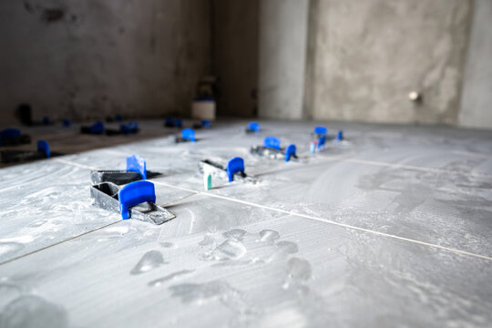 Grey floor tiles installing in a new house or apartment, showing clips and wedges of a tile leveling system ensuring an even surface during the renovation process