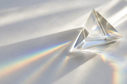 Clear diamond gemstone refracting rainbow light. Faceted crystal prism creating vibrant color spectrum on white surface.