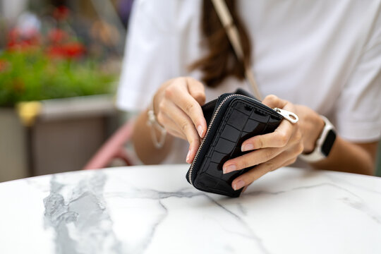 Woman Opening Black Zippered Wallet at Marble Table. Closeup of a woman opening a glossy black zippered wallet above a white marble table while wearing a smartwatch.