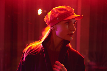 Profile portrait of a stylish young woman in a newsboy cap illuminated by vibrant red neon light at night © Maksim