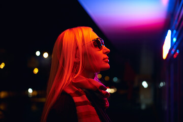 Young woman in sunglasses profile portrait lit by neon city lights at night © Maksim