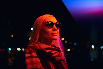 Young woman in sunglasses profile portrait lit by neon city lights at night © Maksim