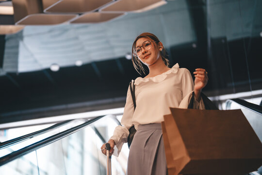 Young adult business woman holding shopping bags standing on escalator.