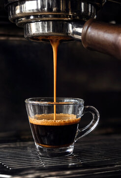 Closeup of freshly brewed espresso coffee pouring into a clear glass cup from machine