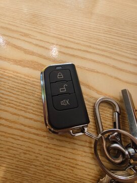 A black car remote key fob attached to a metal keychain resting on a light-colored wooden table