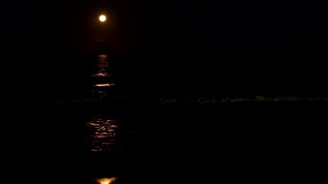 Strawberry full moon rises over ocean throwing moonlight line over surface