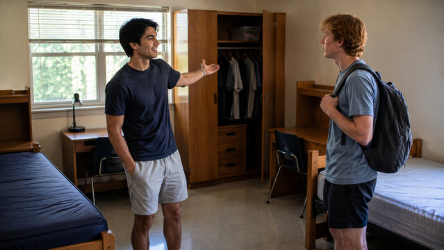 Returning student showing newcomer around dorm room candid photo 