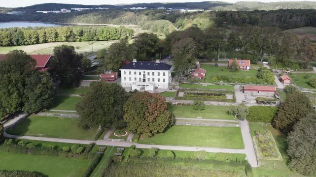 Aerial drone view of Rada Sateri historic manor estate with formal gardens and surrounding parkland. White manor house stands among trees, pathways and landscaped grounds near Radasjon Lake