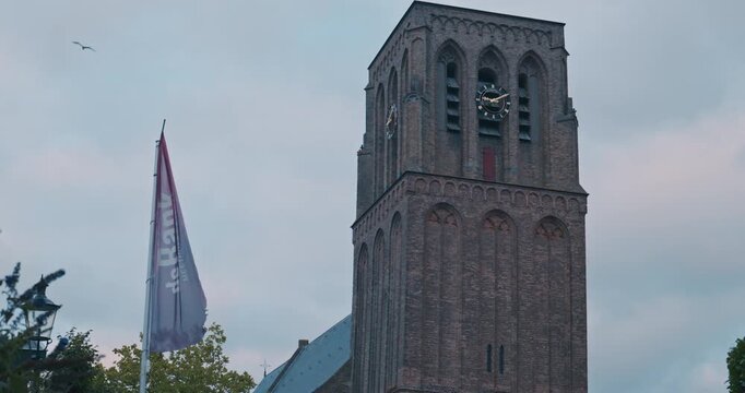 Tall brick tower with clock faces and arched windows against overcast sky clouds