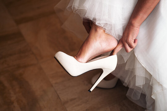 Bride adjusts a white high heel shoe beneath layers of tulle and a wedding dress, capturing a quiet, elegant moment of preparation, anticipation and bridal detail before the ceremony.