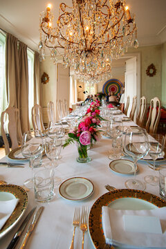 Long formal dining table set for a luxury banquet or wedding reception with crystal chandeliers, pink floral centerpieces, fine china and glassware creating an elegant, celebratory atmosphere.