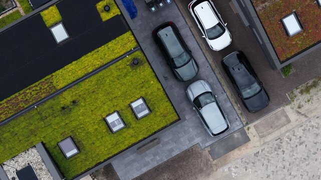 Top down aerial view of modern sustainable houses with living green roofs, solar panels, skylights, and cars parked in the driveway, showing an eco friendly neighborhood concept