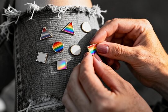 Hands pinning rainbow pride pins on denim
