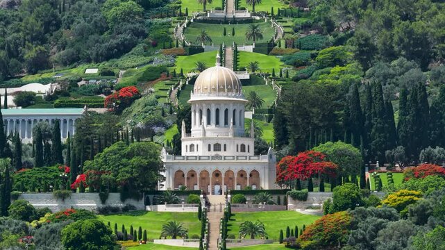 A steady telephoto shot capturing the symmetrical architecture and golden dome of the historic Bahai temple framed by the lush green manicured terraces on Mount Carmel.