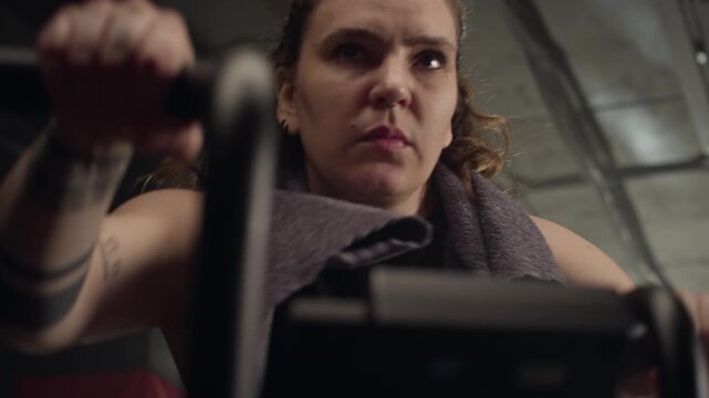 POV close up of young Caucasian woman training intensely on stationary air bike in gym, breathing heavily. Perfect for promoting cardiovascular health, fitness apps, and active lifestyle campaigns