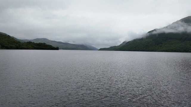 High drone view of Loch Lomond showing tranquil water forests and green Highland hills in The Trossachs National Park.