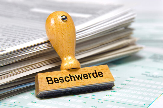 An einem Stapel mit Papier lehnt ein Holzstempel mit dem Aufdruck: Beschwerde
