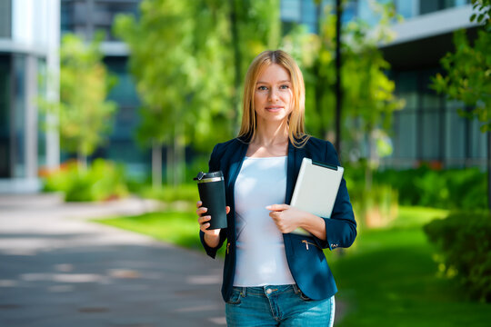 Smiling Businesswoman Using Wireless Earbuds and Holding a Tablet in a Modern City Park