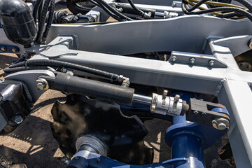 Fototapeta premium Agricultural machinery disc harrow depth control hydraulic cylinder. Modern farm cultivation equipment part on grey frame with stroke limiter clips and industrial vehicle technical details.