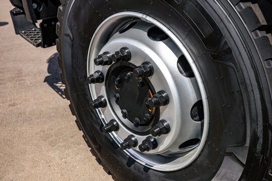 Heavy truck wheel steel rim with black lug nuts and hub cap. Modern commercial transport vehicle tire axle section closeup view with heavy duty industrial cargo tractor engineering details.