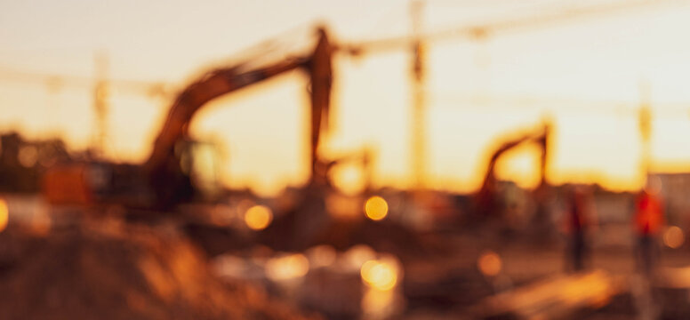 Blurred image of construction equipment at a sunset, showcasing cranes and machinery operating on a construction site, creating an urban landscape atmosphere.
