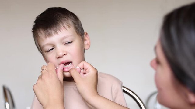Mother cleans boy teeth with dental floss in slow motion. Close up shows gentle oral hygiene routine and healthy family dental care.