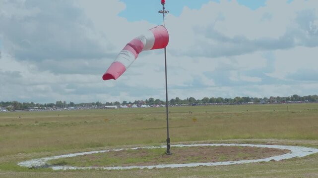 Red and white windsock on airfield under cloudy sky