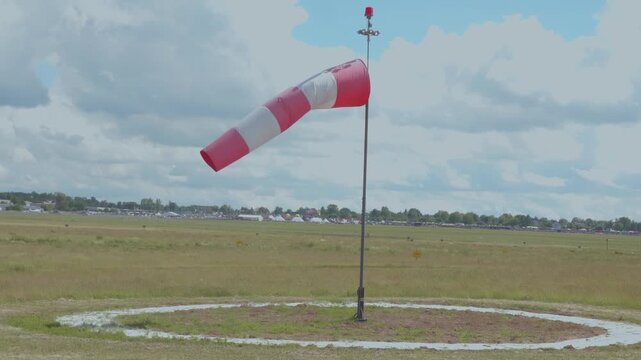 Red and white windsock on airfield under cloudy sky
