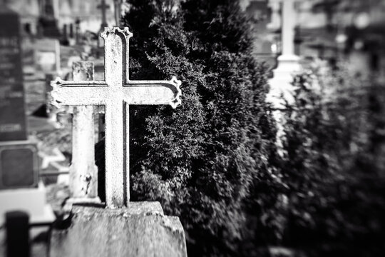 Old iron cross in cemetery. Black and white image. Selective focus, tilt shift, partly blurred. Ancient tombstone detail.