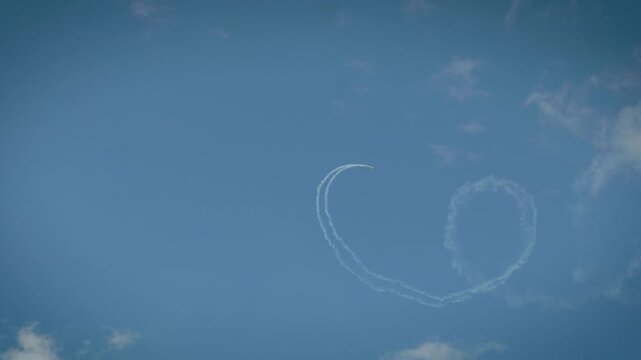 Two planes completing a loop maneuver with smoke trails in a cloudy blue sky.