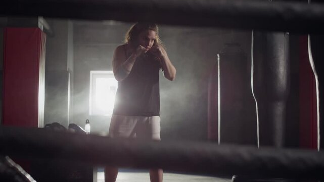 Caucasian young woman shadow boxing inside boxing ring, throwing punches in athletic gym. Ideal for fitness brand commercials, gym promotions, and motivational sports marketing campaigns