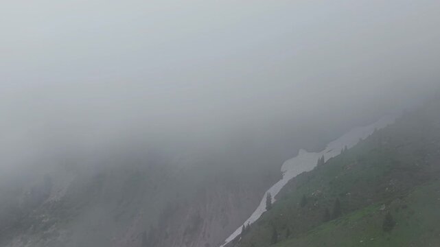 Fog envelops a mountainous landscape, gradually revealing a winding river and patches of greenery as visibility improves, showcasing the serene beauty of nature in a remote area