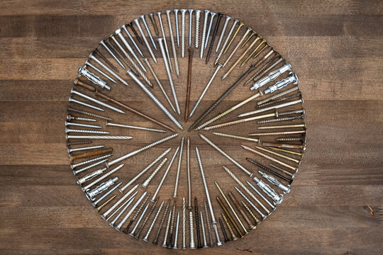 Circle made of various screws and nails on brown wood texture. Industrial flat lay. Carpentry still life.