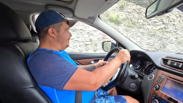A focused man drives a passenger car along a narrow Georgian route, keeping both hands on the steering wheel while the interior scene supports road safety, mobility, transport, and driver training