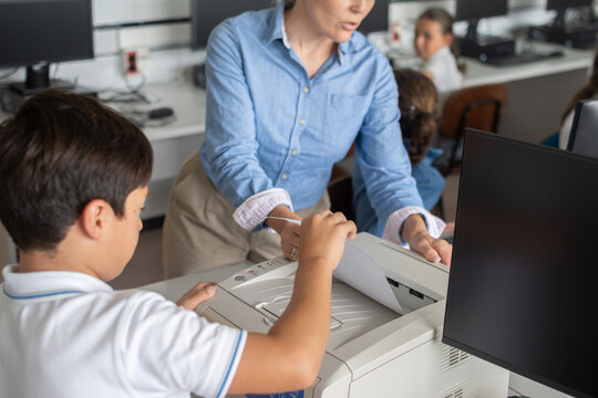 Teacher helping student use printer in school computer classroom