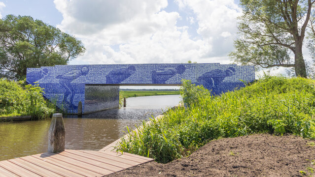 Famous monument Blue tiled bridge of the Eleven Cities Ice Skating tour over calm canal with wooden dock and lush green riverbank