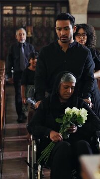 Family, church and woman in a wheelchair for funeral with flowers for memorial, widow or service. Group, arrive or senior person with disability in chapel for christian religion, mourning or sad