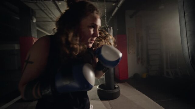 Young Caucasian woman boxing intensely, punching heavy bag in gym. Clip suitable for fitness brand commercials, motivational videos, and mental health campaigns promoting stress relief
