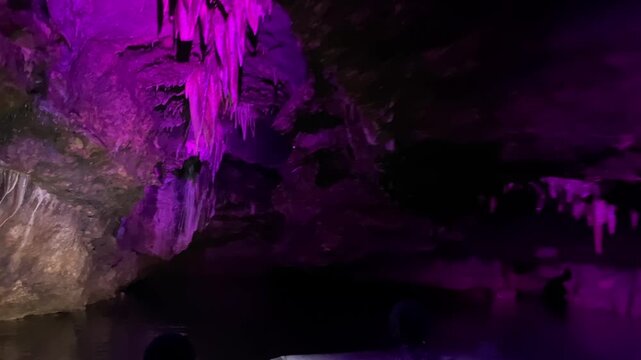 A tour boat follows the underground canal through Prometheus Cave in Georgia, passing illuminated stalactites and dark chambers for geotourism promotion, visitor attraction marketing