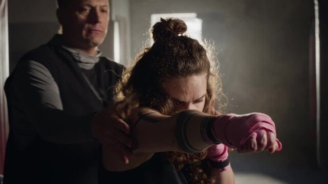 Caucasian middle aged male trainer correcting boxing punch posture of Caucasian young woman in gym. Clip is perfect for fitness center marketing and personal training advertisements