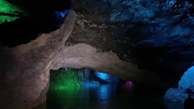 Passengers navigate a narrow water passage inside Prometheus Cave, where red illumination reflects on the canal and limestone ceiling, presenting underground attraction operations