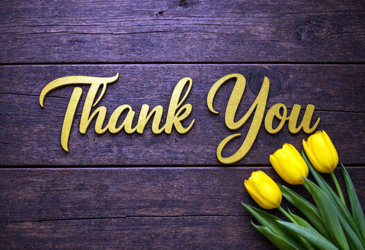 Beautiful yellow tulips beside thank you golden text on rustic wooden background